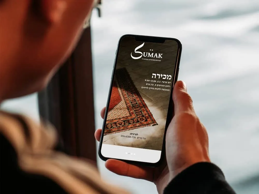 יד מחזיקה טלפון עם מודעת מכירה של שטיחים ולוגו סומאק על המסך
